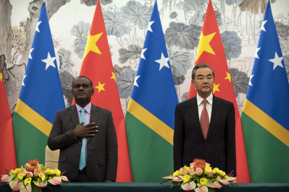 Solomon Islands Foreign Minister Jeremiah Manele, left, and Chinese Foreign Minister Wang Yi stand during the Solomon Islands national anthem at a ceremony to mark the establishment of diplomatic relations between the Solomon Islands and China at the Diaoyutai State Guesthouse in Beijing, Saturday, Sept. 21, 2019. (AP Photo/Mark Schiefelbein, Pool)