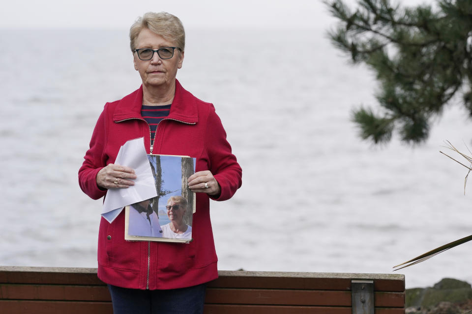 Diane Ostrander poses for a photo, Thursday, Jan. 20, 2022, in Kirkland Wash., while holding a picture of her and her son, who is now in a behavioral health hospital, during happier times together. For months, Ostrander worried desperately about her son as he faced a mental-health crisis, but the police Ostrander begged for help relayed a consistent message: A new state law meant officers couldn't take her son to get help against his will, even though mental health professionals and a judge ordered it. The park bench behind her on the Lake Washington waterfront was one fo the last places Ostrander said she and her son were able to spend peaceful time together. (AP Photo/Ted S. Warren)