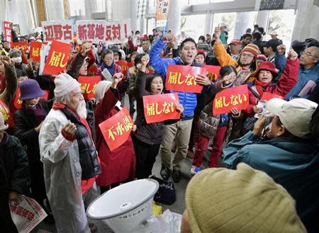 Protesters holding banners raise their fists as they shout slogans during a rally against the relocation of a U.S. military base, at the entrance of the Okinawa prefectural government office building, in Naha on the Japanese southern islands of Okinawa, in this photo taken by Kyodo December 27, 2013. REUTERS/Kyodo