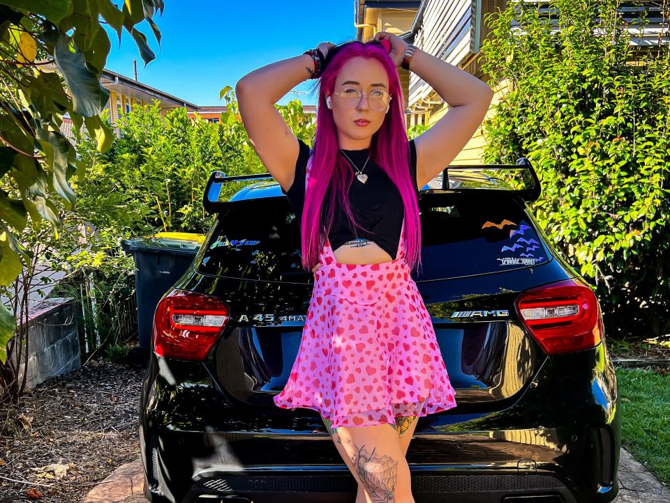 Raven Inferno pictured wearing a pink skirt and shoes in front of a car with pink car
