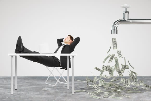 A man in a suit resting in a chair as money flows out of a faucet behind him.