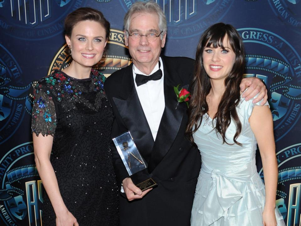 Emily and Zooey Deschanel standing next to Caleb Deschanel who is holding an award