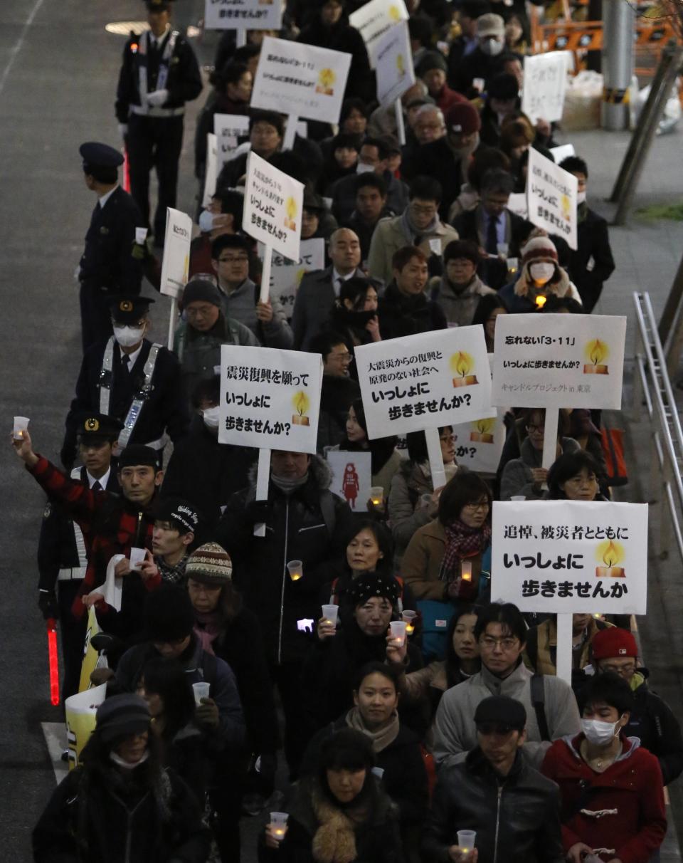 People hold electric candles as they participate in a vigil to pay tribute to the victims of the March 11, 2011 earthquake and tsunami and to protest against nuclear power, in Tokyo March 11, 2014. Placards read "let's walk together" and " 3.11 is not over". (REUTERS/Yuya Shino)