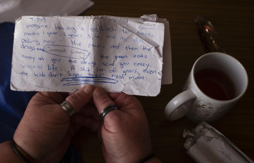 Carmall Casey reads a note she wrote while sitting at her home in Black River, Tasmania, Australia, Wednesday, July 24, 2019. One day, she scrawled her anguish on a tattered envelope. "Imagine having a toothache for weeks, months 1 year, 2 years, 3, 4, and it's still aching now ... the pain eats away at you, the drugs send you crazy," she wrote. "Even the kids don't know their real mum." (AP Photo/David Goldman)