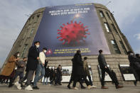 People wearing face masks as a precaution against the coronavirus walk under a banner emphasizing an enhanced social distancing campaign in front of Seoul City Hall in Seoul, South Korea, Wednesday, Nov. 25, 2020. The banner reads: "We have to stop before COVID-19 stops everything." (AP Photo/Ahn Young-joon)