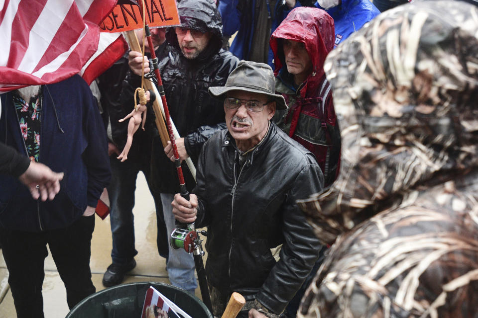 A man with a flag that had a doll with a noose around its neck attached to it grimaces as he comes to the front of the stage during a protest against the state's stay-at-home order at the Michigan Capitol in Lansing, Mich., Thursday, May 14, 2020. (J. Scott Park/Jackson Citizen Patriot via AP)