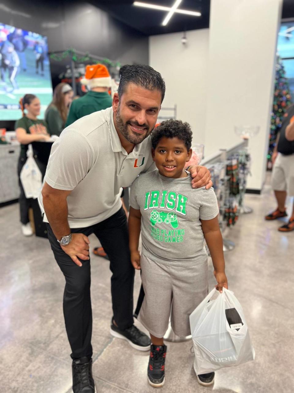 UM baseball coach J.D. Arteaga is shown with a child that took part in the Hurricanes Team Store Holiday Shopping Spree on Monday, Dec. 11, 2023 to honor the legacy of late UM football player Bryan Pata.