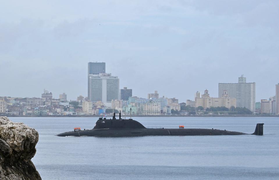 A submarine on the water's surface with a city skyline in the background.