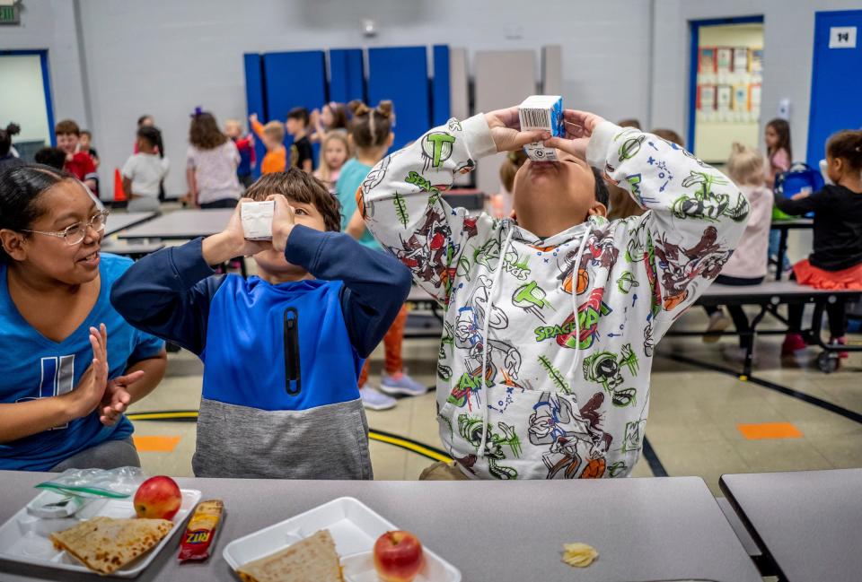 Two students are cheered on by another while having a race to finish their cartons of milk during a lunch at Wilcox Elementary School in Holt on Wednesday, Nov. 8, 2023. Students at the school are supplied with free lunches as part of the Michigan School Meals project, which makes breakfast and lunch free for all students in public schools.