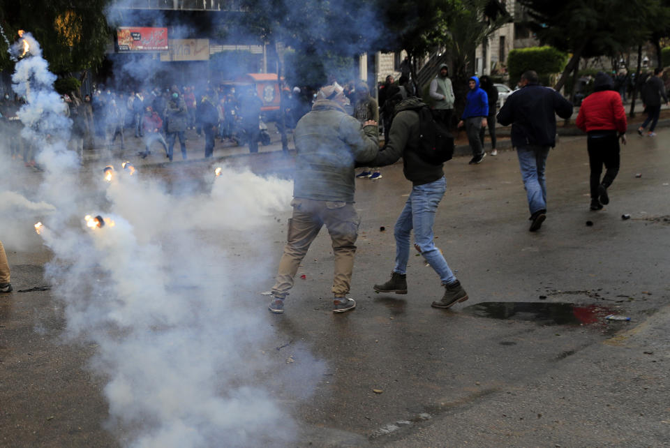 Protesters run from tear gas canisters during a protest against deteriorating living conditions and strict coronavirus lockdown measures, in Tripoli, north Lebanon, Thursday, Jan. 28, 2021. Violent confrontations for three straight days between protesters and security forces in northern Lebanon left a 30-year-old man dead and more than 220 people injured, the state news agency said Thursday. (AP Photo/Hussein Malla)