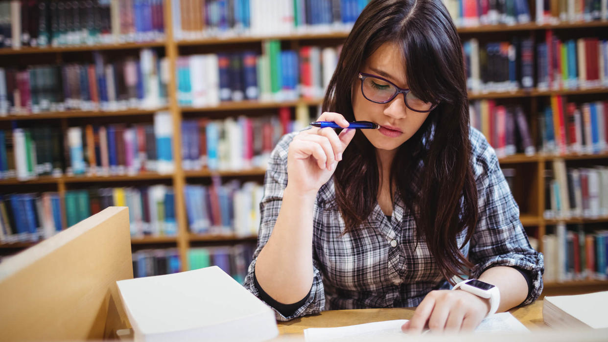 Thoughtful female student looking at notes in library.