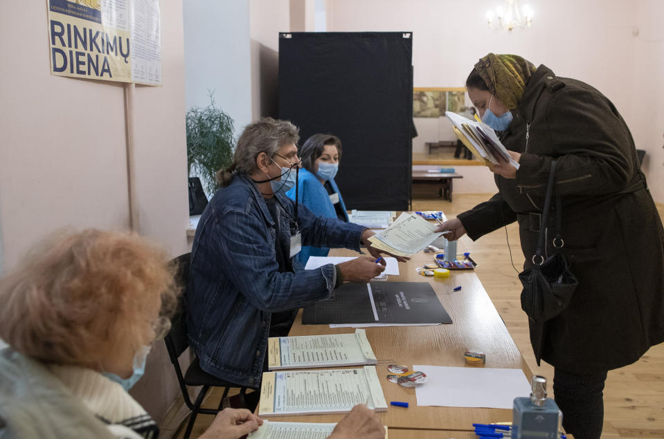 A Lithuanian woman, wearing face mask to protect against coronavirus, arrives at a polling station during parliamentary elections in Vilnius, Lithuania, Sunday, Oct.11, 2020. Polls opened Sunday for the first round of national election in Lithuania, where voters will renew the 141-seat parliament and the ruling four-party coalition is widely expected to face a stiff challenge from the opposition to remain in office. (AP Photo/Mindaugas Kulbis)