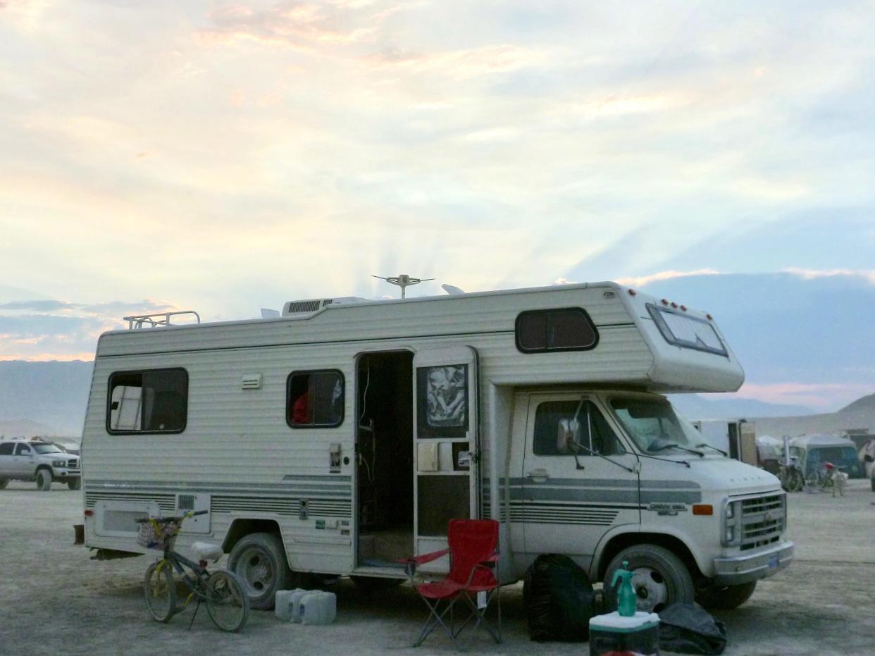 a white RV parked at Burning Man in the desert with a colorful sky in the background