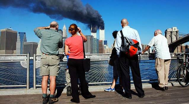 Pedestrians on the waterfront in Brooklyn look across the East River to the burning World Trade Centre towers. Picture: Getty