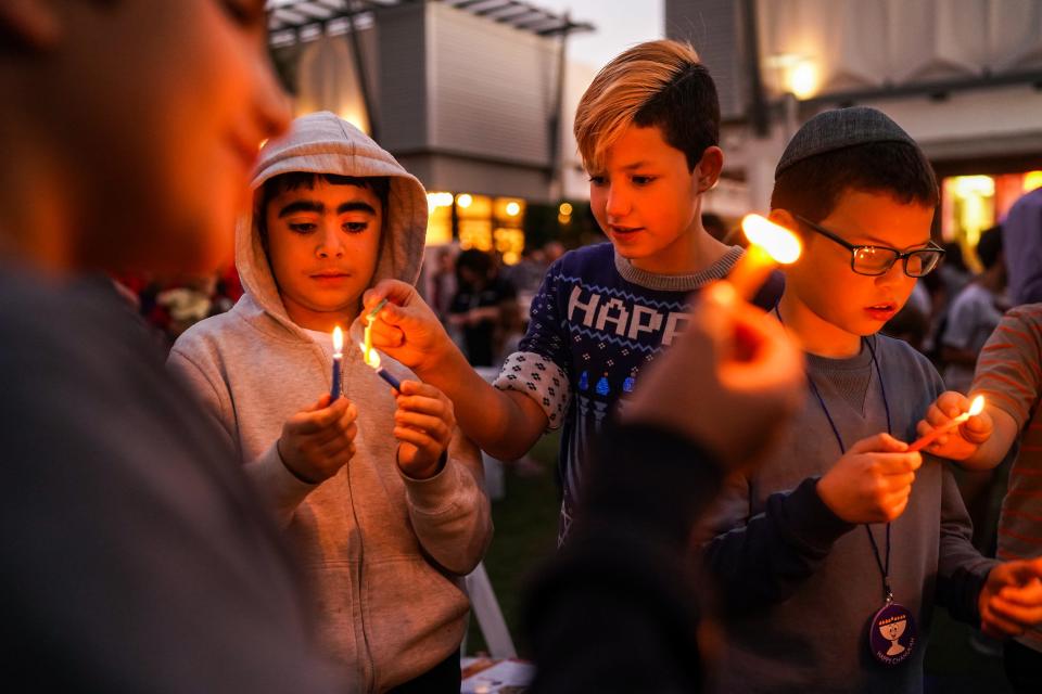 From left, Issacher Shakhmurov, 9, Ely Teitelbaum, 10, and Yossi Levertov, 9, light their candles during a celebration for the first night of Hanukkah at the Biltmore Fashion Park on Sunday, Nov. 28, 2021, in Phoenix. The event was hosted by Chabad Lubavitch of Arizona.