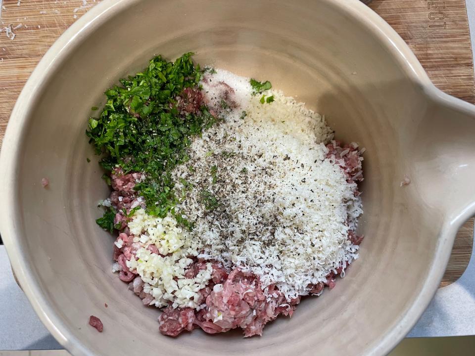 herbs, cheese, onion, garlic, and ground meats in a ceramic mixing bowl