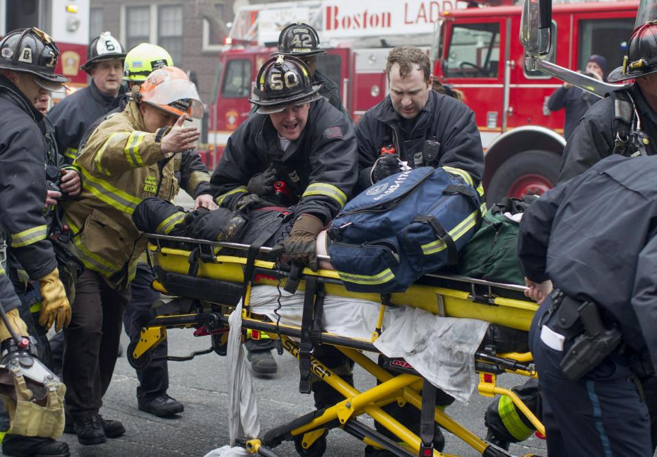 Firefighters and emergency medical personnel rush a firefighter from the scene of a multi-alarm fire at a four-story brownstone in the Back Bay neighborhood near the Charles River, Wednesday, March 26, 2014, in Boston. Boston EMS spokesman Nick Martin says four people, including at least three firefighters, have been taken to hospitals. (AP Photo/Scott Eisen)