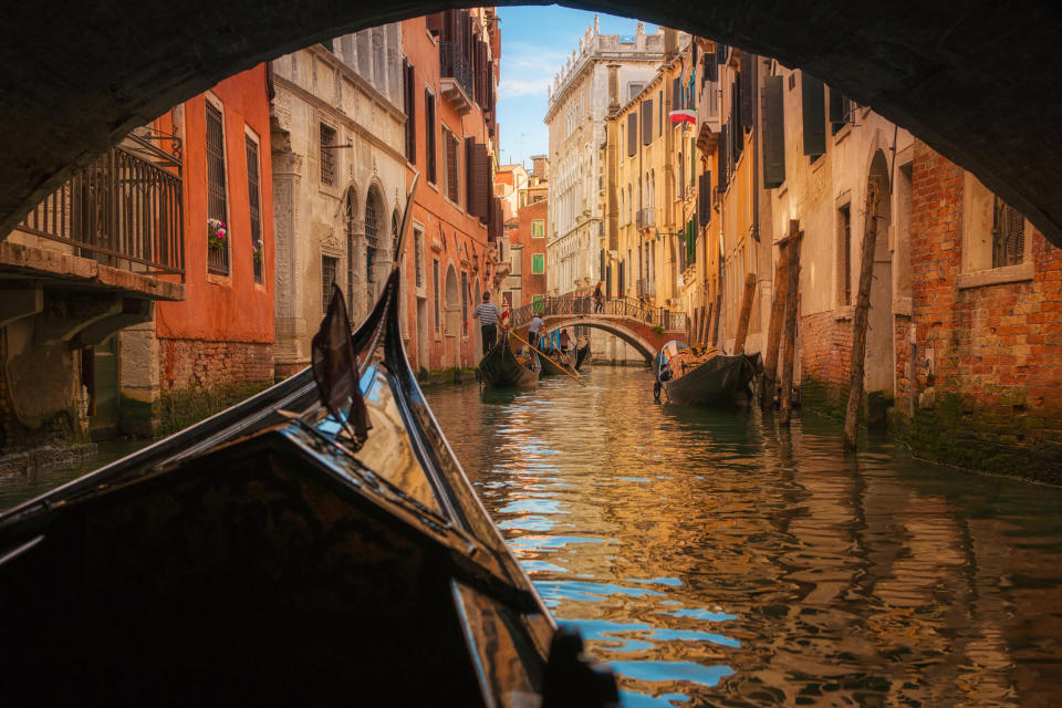 View from a gondola on a narrow Venetian canal with bridges and ancient buildings