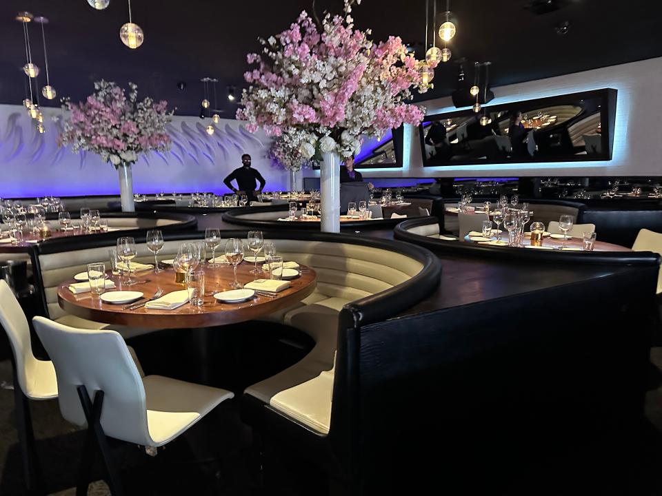 A steak house with black and white seating with circular wooden  table with pink and white flowers