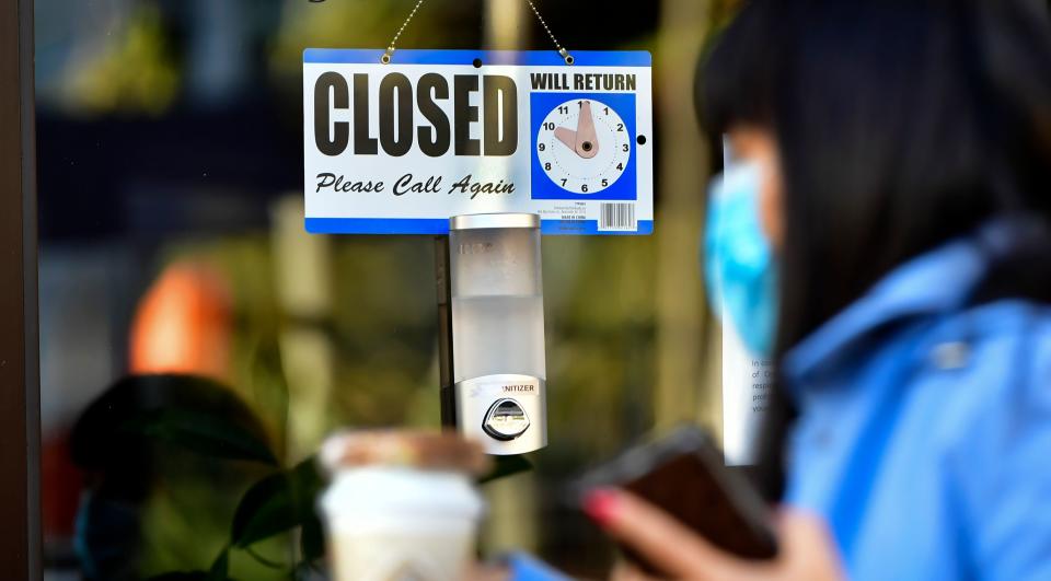 A pedestrian wearing her facemask and holding a cup of coffee walks past a Closed sign hanging on the door of a small business in Los Angeles, California on November 30, 2020. - Los Angeles County's new stay-at-home restrictions took effect on November 30, 2020, one day after the county reported more than 5,000 new COVID-19 cases. (Photo by Frederic J. BROWN / AFP) (Photo by FREDERIC J. BROWN/AFP via Getty Images)