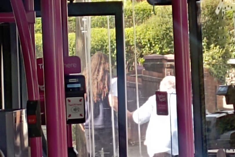 A bus driver helps an elderly patient across the road after she left his service