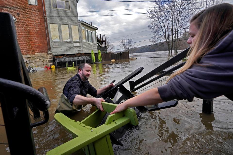 Nathan Sennett hands furniture to Tori Grasse as they work in hip-deep water on the patio of the Quarry Tap Room, Tuesday, Dec. 19, 2023, in Hallowell, Maine. Waters continue to rise in the Kennebec River following Monday's severe storm. (AP Photo/Robert F. Bukaty)