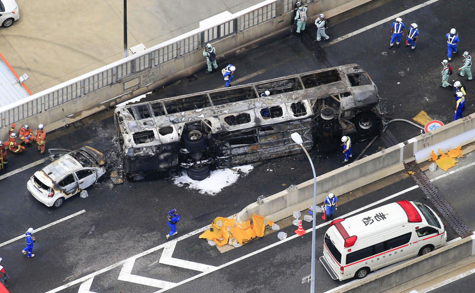 Investigators work near the overturned bus on a high way in Toyoyama, Aichi prefecture, central Japan Monday, Aug. 22, 2022. A passenger bus crashed into a dividing strip, overturned to its side and caught fire on an expressway in central Japan on Monday, leaving two people burned to death and slightly injuring seven others, police said. (Kyodo News via AP)