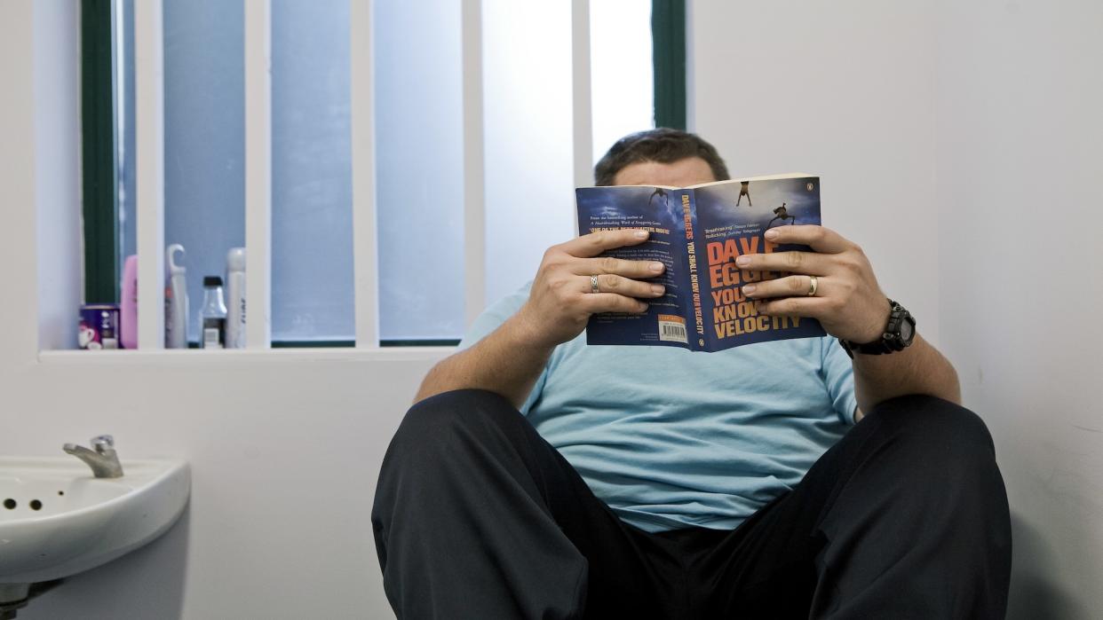  A man reads a book in a jail cell. 
