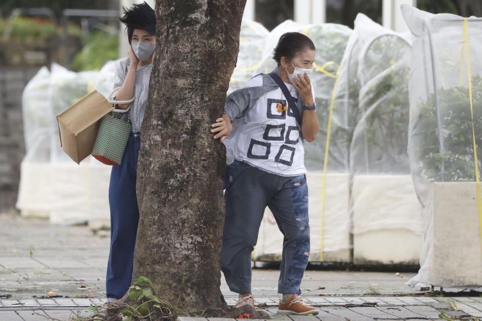 Pedestrians hold a tree to protect themselves from strong winds as Typhoon Hinnamnor hits in Naha, Okinawa prefecture, Japan Sunday, Sept. 4, 2022. (Kyodo News via AP)