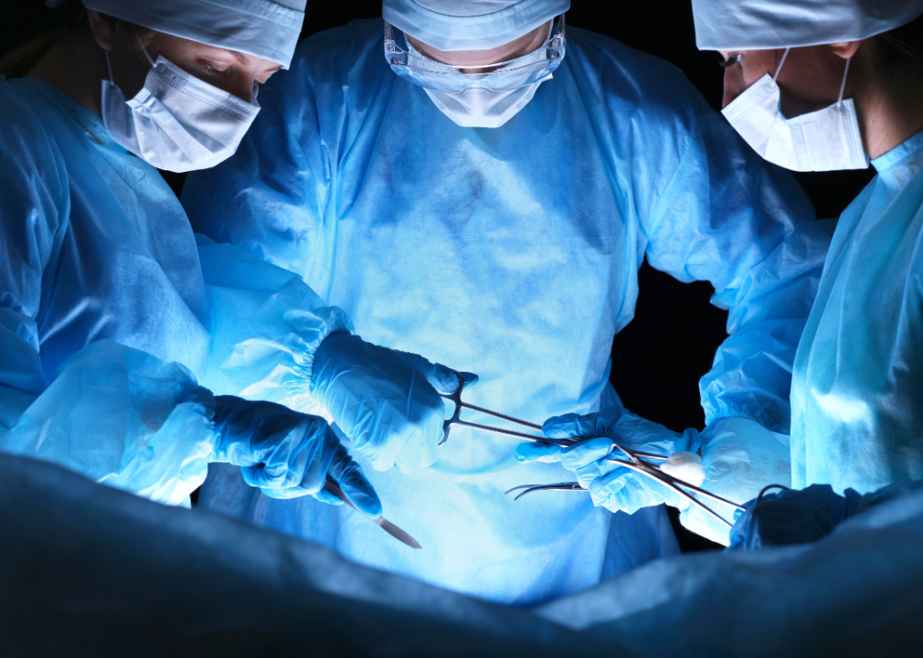 A close-up of three surgeons holding different tools over an operating table.