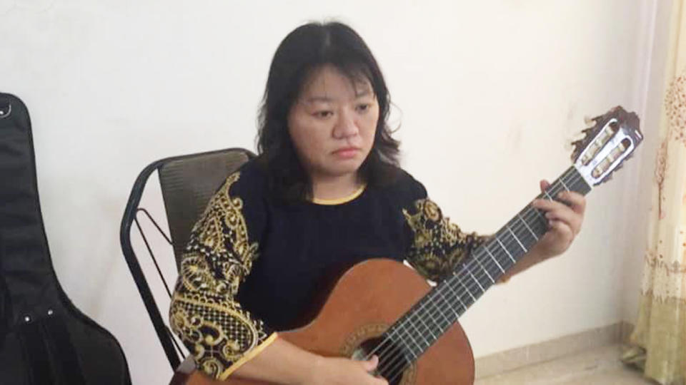 Pham Doan Trang sits in a chair holding a guitar in her lap.