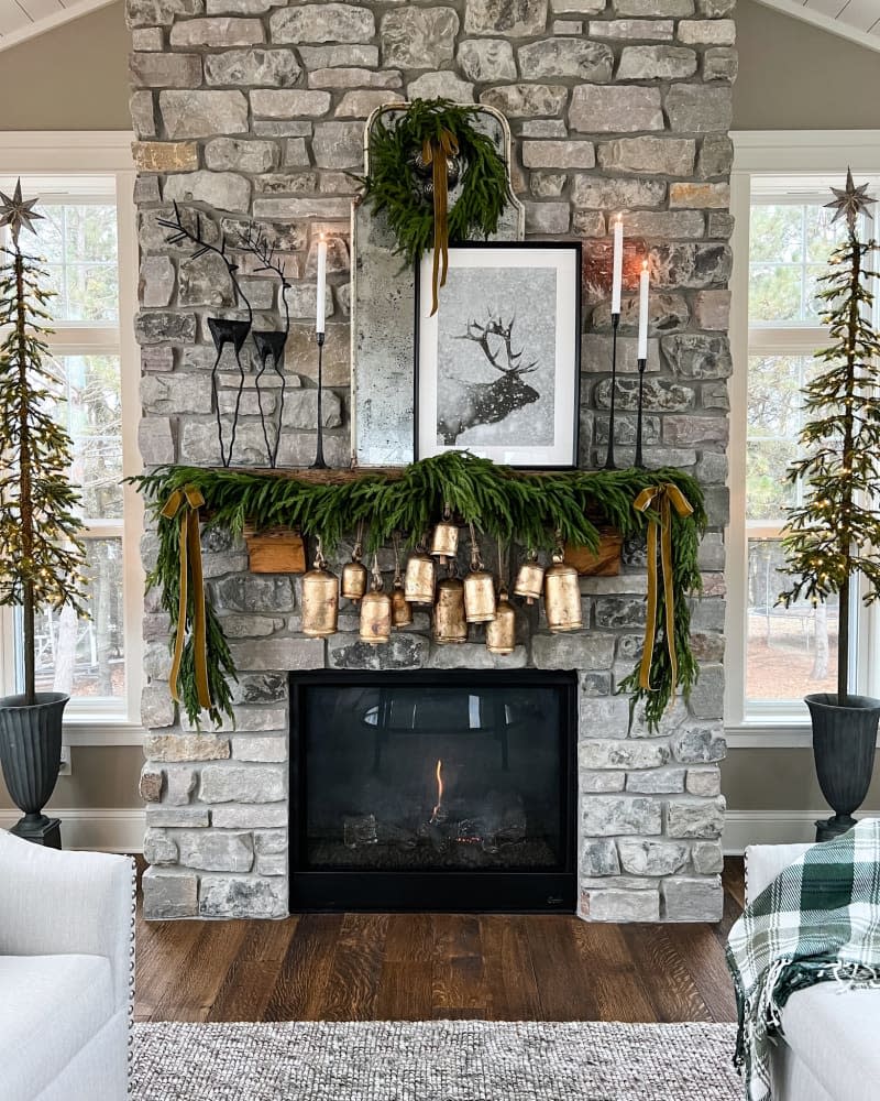 Fireplace mantel decorated with winter greenery garland and oversized brass bells