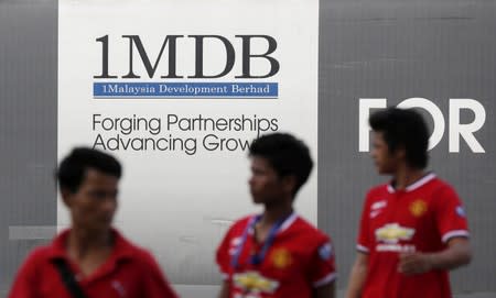 FILE PHOTO: Men walk past a 1Malaysia Development Berhad (1MDB) billboard at the fund's flagship Tun Razak Exchange development in Kuala Lumpur