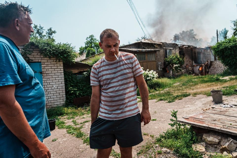 Man smokes a cigarette in front of a house with smoke coming from the roof