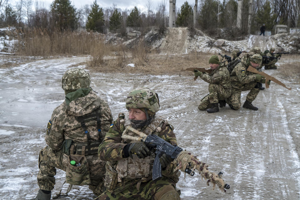 Members of the Kyiv Territorial Defense Force, some holding rifles, attend a training outdoors in an industrial area. 