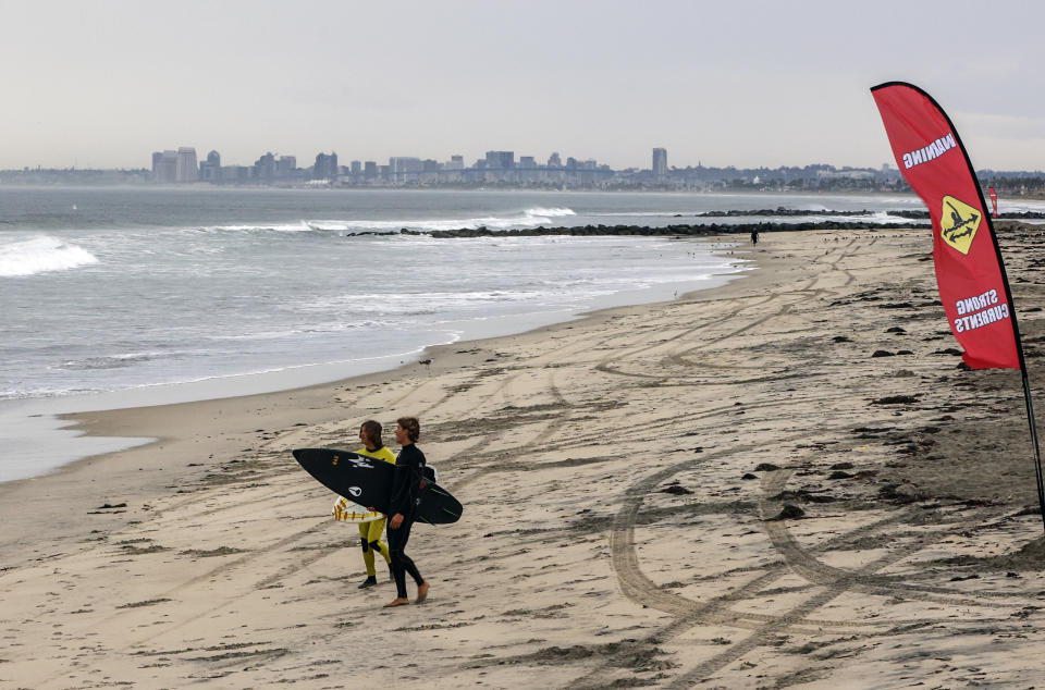 With a strong currents warning flag, surfers head out to waves just north of the Imperial Beach Pier on Friday, Sept. 9, 2022 in Imperial Beach, Calif. A surge of clouds and showers associated with Tropical Storm Kay off Mexico's Baja California peninsula knocked the edge off temperatures in Southern California at times but also were a potential problem for solar generation. The storm was downgraded from a hurricane Thursday evening. (Eduardo Contreras/The San Diego Union-Tribune via AP)