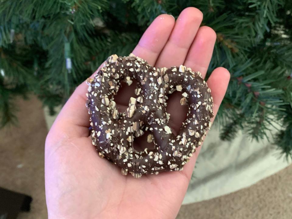 hand holding trader joes chocolate-covered pretzels with almonds in front of tree