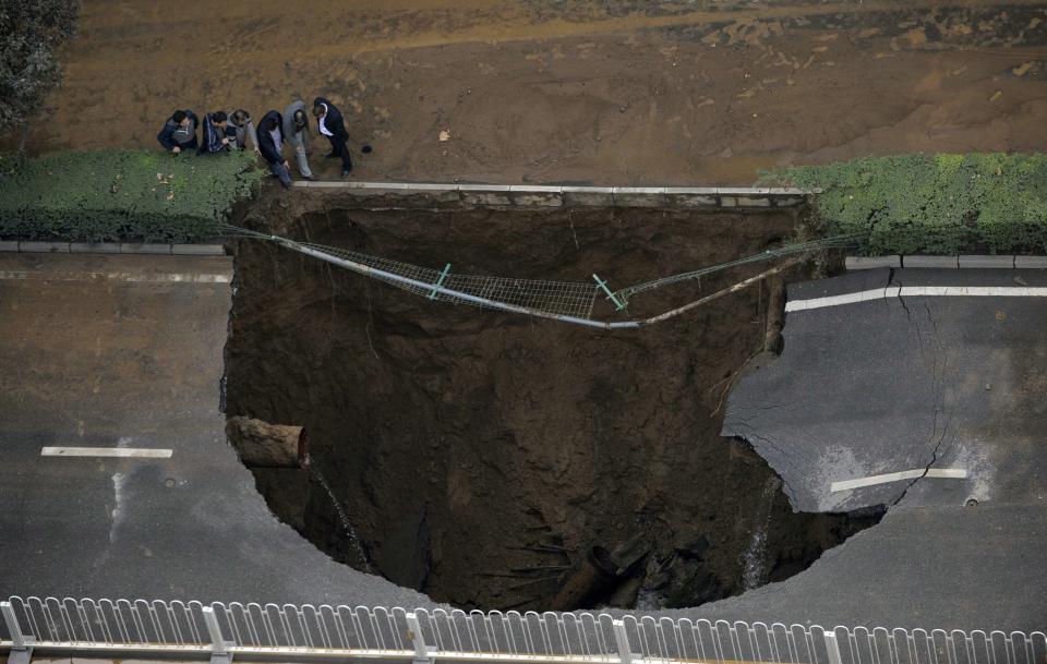 People look at a large sinkhole on a street after a water pipe broke underneath it in Xi'an