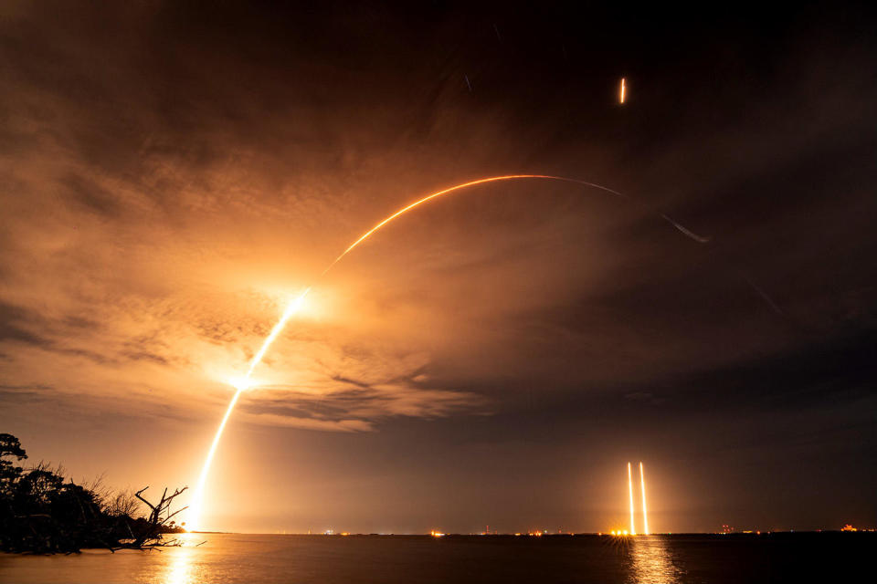 A time exposure captures the fiery trail of a SpaceX Falcon Heavy rocket during blastoff from the Kennedy Space Center, along with the plumes from two side  boosters as they descended to side-by-side landings at the Cape Canaveral Space Force Station. / Credit: Michael Cain/Spaceflight Now