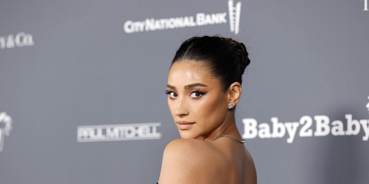 shay mitchell at the baby2baby gala on the red carpet with her hair up and wearing a black off the shoulder gown