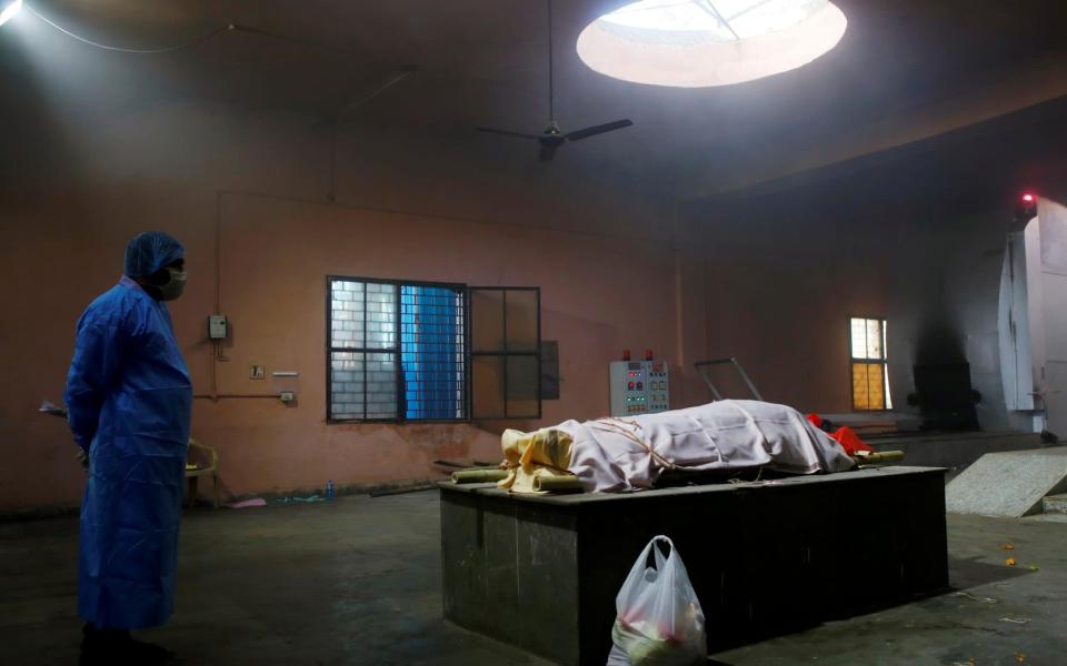 Alone in an empty room, a family member dressed head-to-toe in personal protective equipment waits with the body of their relative, a victim of Covid-19, before the cremation - REUTERS/Adnan Abidi