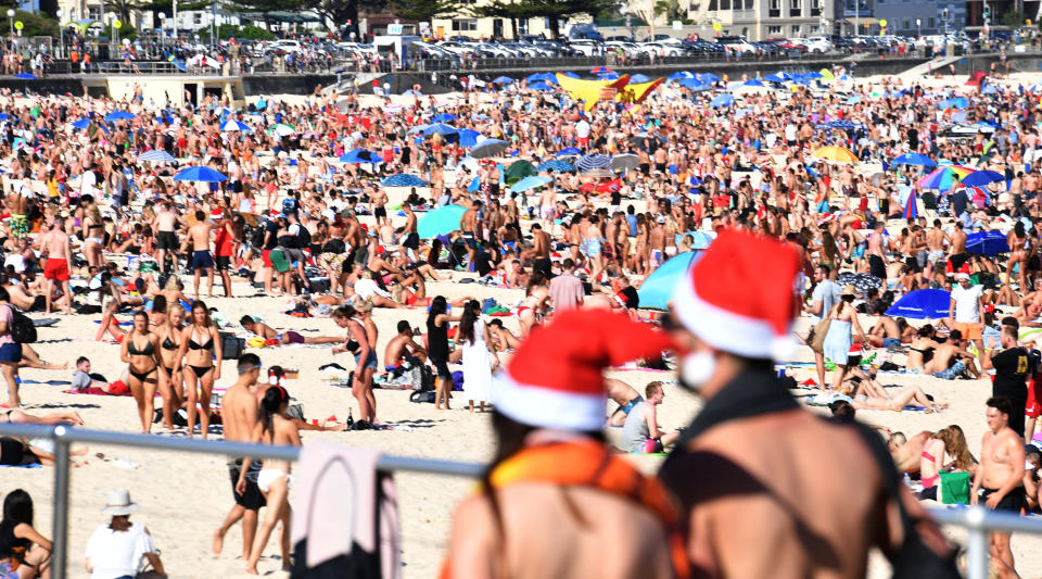 Bondi Beach at Christmas with people on the sand and wearing Santa hats on the publicn holiday.