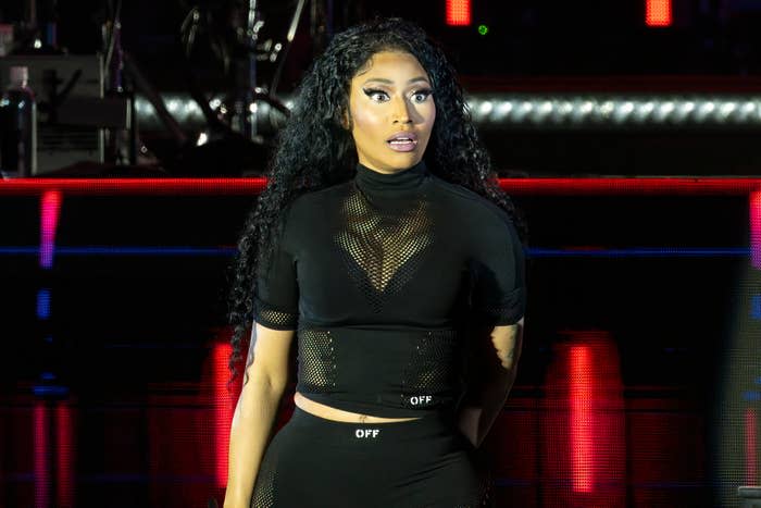 Nicki Minaj on stage wearing a black, sheer crop top and matching leggings, performing with an expressive look