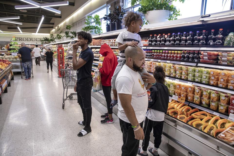 In this Thursday, Aug. 15, 2019, photo, Christopher "Mad Dog" Thomas, carries his son, Rian Gatewood-Hillestad, while shopping at Pete's Market in Chicago's Garfield Neighborhood. Thomas, who grew up in the Altgeld Gardens neighborhood on Chicago's South Side, said he has suffered from "'food desert eating disorder,' where all you can afford to eat is candy." Thomas and his wife, make a weekly trip outside their neighborhood to this store, which his wife describes as "the black or Hispanic Whole Foods." (AP Photo/Amr Alfiky)