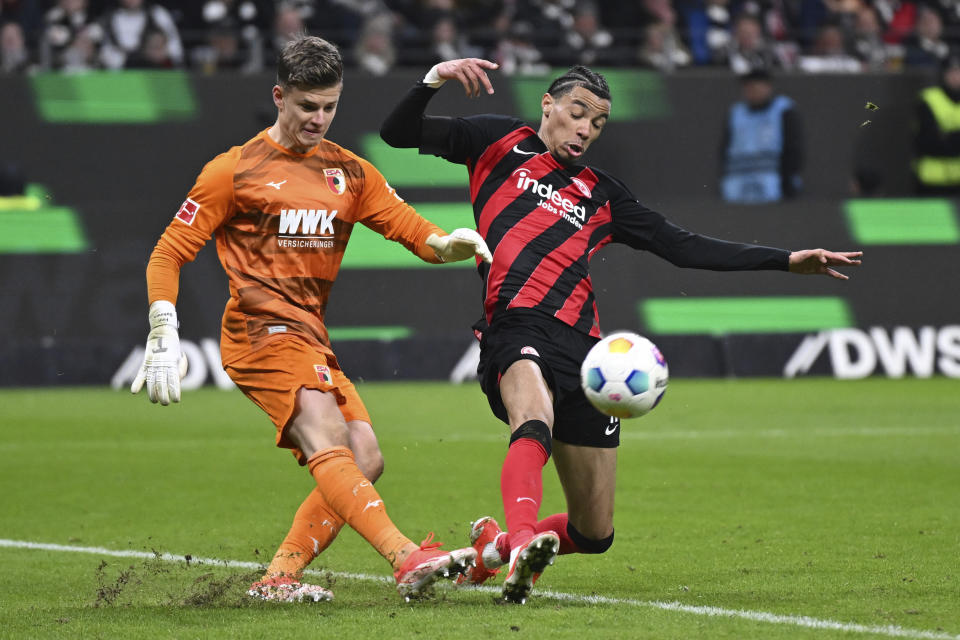 Augsburg goalkeeper Finn Dahmen, left, clears the ball past Frankfurt's Hugo Ekitike during the German Bundesliga soccer match between Eintracht Frankfurt and FC Augsburg, in Frankfurt, Germany, Friday, April 19, 2024. (Arne Dedert/dpa via AP)