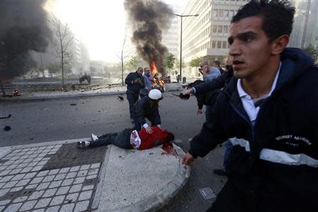 People run to help a wounded man as smoke rises from the site of an explosion in Beirut's downtown area December 27, 2013. The explosion rocked the Lebanese capital on Friday, causing an unknown number of casualties.The blast was heard across the city and a plume of black smoke was seen rising in the downtown business district near the Phoenicia Hotel. REUTERS/Jamal Saidi