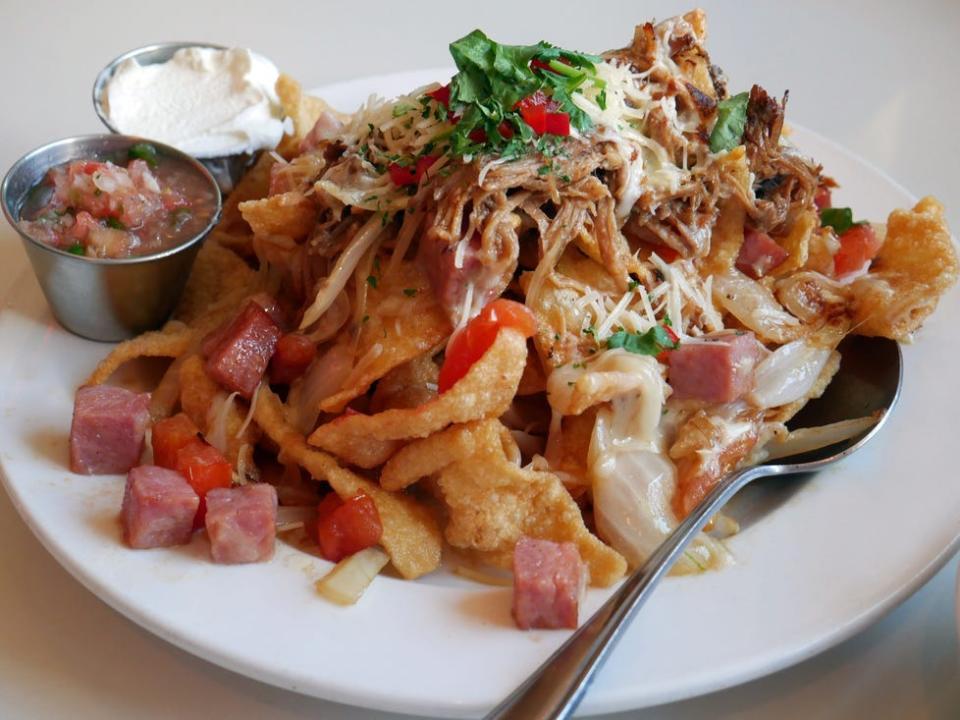 Kalua pork nachos on a white plate with salsa and sour cream on the side