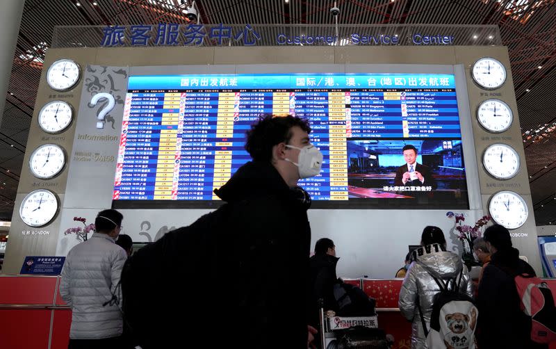 A foreign traveller wearing a mask walks past a departures information board at Beijing International Airport in Beijing