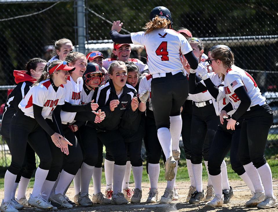 The Hudson High School softball team waits for teammate Caitlin Cassidy (4) to come in for a landing on home plate after Cassidy's solo home run in the Hawks 14-4 victory over Dracut in the opening round of the Sheryl Jones Tournament at Hudson High School on April 20.