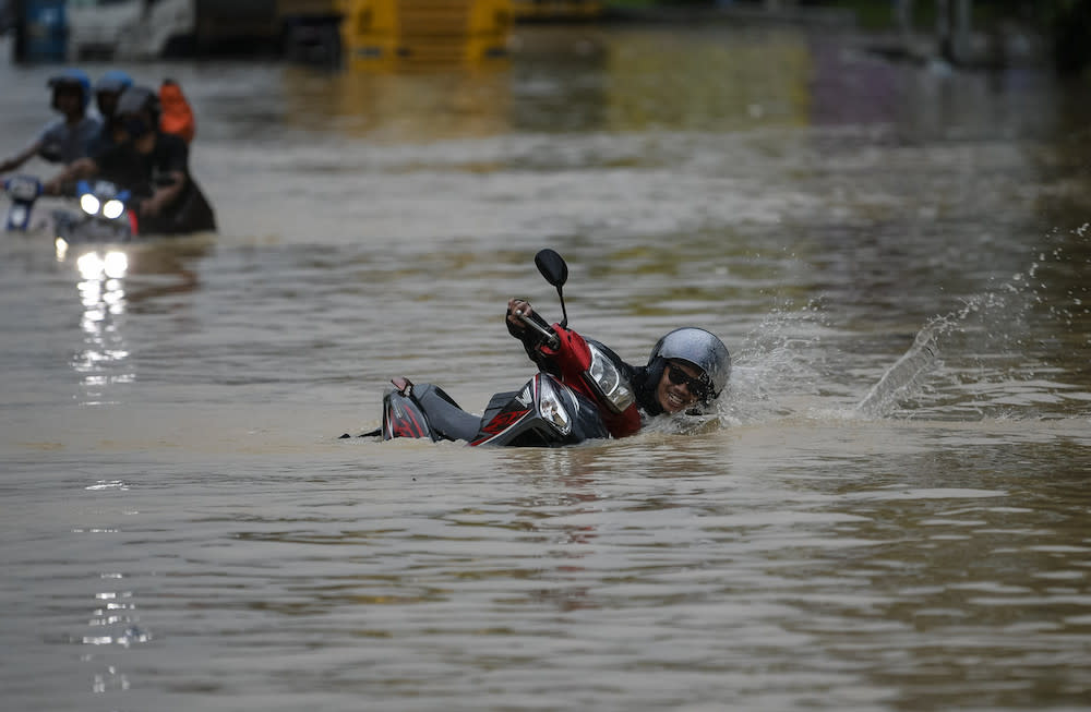 A motorcyclist falls while navigating the flooded Federal Highway, December 18, 2021. — Bernama pic